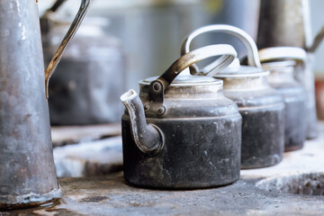 Close-up of old, blackened kettles with worn handles sitting on a rustic stovetop in an open kitchen, commonly used for communal cooking. Turkmenistan
