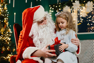 Santa Claus sharing a joyful moment with a little girl as he presents her with a holiday gift