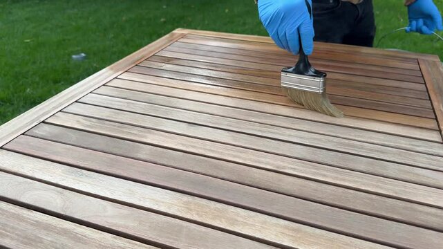 Teak wood table renovation, worker applying protective oil on exterior hardwood furniture