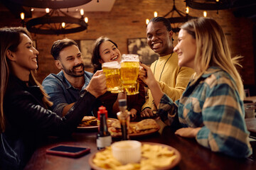 Multiracial group of happy friends having fun and toasting while drinking beer in pub.