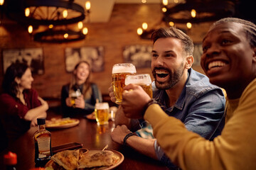 Happy male friends having fun and toasting while drinking beer in pub.
