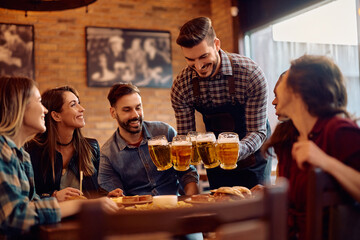 Happy waiter serving beer to group of guests in bar.