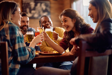 Young cheerful people toasting while celebrating their friendship in pub.