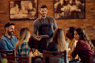 Young waiter taking order from group of customers while working in pub.