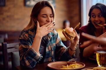 Happy woman eating in hamburger with her friends in pub.