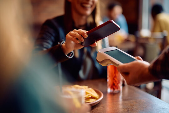Close up of woman using smart phone while paying to waiter in pub.