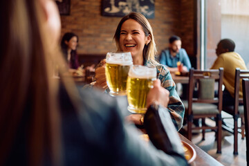 Cheerful women toasting while drinking beer in pub.