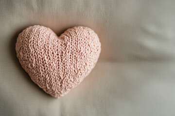 A close-up of a heart crafted from delicate pastel  yarn, showcasing intricate knitted patterns and loops, set against a neutral beige backdrop for a warm, minimalist, and cozy feel