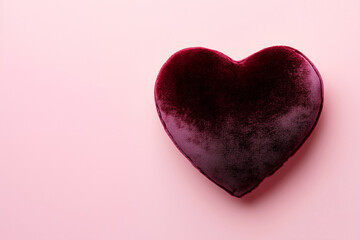 A heart-shaped design in rich burgundy velvet, showcasing detailed fabric texture illuminated by gentle lighting, set against a smooth pastel pink backdrop for a sophisticated and romantic aesthetic.