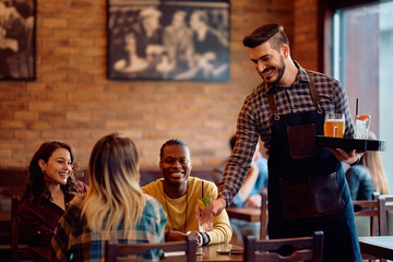 Happy waiter serving multiracial group of friends in bar.