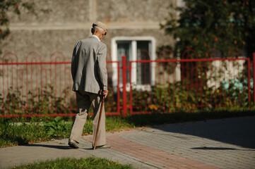 stylish old man in a gray suit, gray cap, gray shoes and a cane walks down the street
