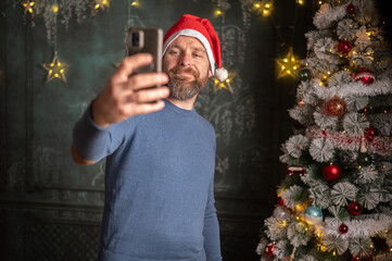 Young  man using smartphone by christmas tree at home