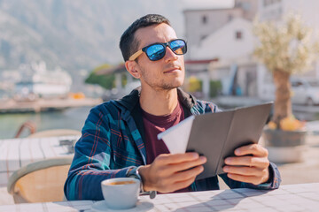 A man sits at a seaside cafe, sipping coffee while thoughtfully reading the menu.