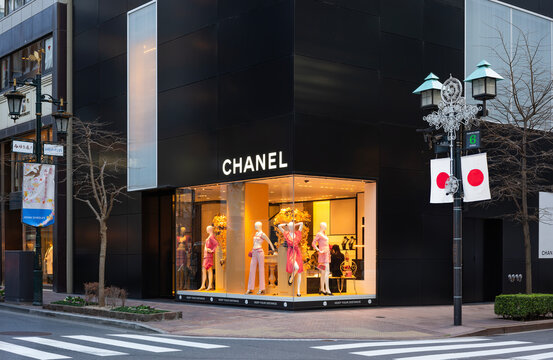 tokyo, ginza &ndash; jan 08 2023: Chanel store on the corner of namiki and miyuki streets with mannequins dressed in haute couture standing in a lit window and with lampposts adorned with the japanese flag.
