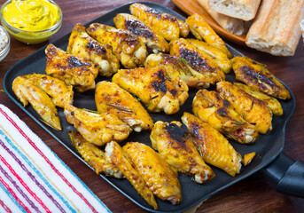 Picture of dish of tasty fried chicken wings served in black pan on table