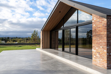 A modern New Zealand farmhouse with an exterior of raw red brick, and glazing on the front facade that opens up to views across farmland, large black windows, and doors.