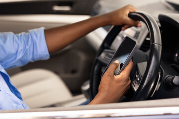 Positive black male driver holding mobile phone while driving nice auto, using new mobile application for navigation going on vacation or making summer trip, stuck in traffic jam, profile side view