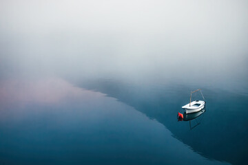 Naklejka premium Minimalist seascape featuring a small white boat on calm water with dense fog, pink and blue reflections, creating a serene and mysterious atmosphere