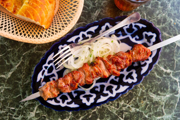 On plate is roasted lamb kebab cooked on skewer. Dish is complemented with rings of pickled onions and flatbread of white bread