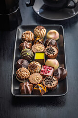 Mix of chocolate pralines on plate on black table.