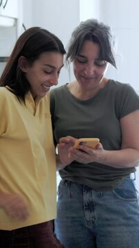 Mother and daughter sharing a moment browsing smartphone. Hispanic, single family