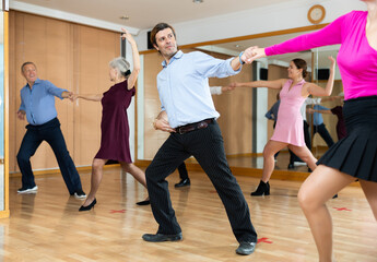 Spirited middle-aged pair training waltz dance during workout session. Pairs training ballroom dance in hall