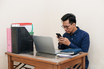 Sa and crying Southeast Asian Man Works while Sitting in front of a laptop and holding handphone at Home office. The Workplace of a Professional Worker, Freelancer or Student. 