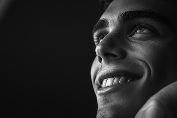 Close up of young smiling man resting chin on palm looking upwards  low key  black and white