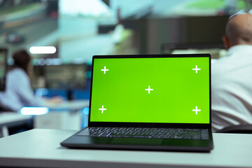 Laptop showing blank greenscreen display in a control center agency, people working with...