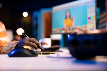 Black remote designer working from well organized home office, retouching photos on dual monitors...