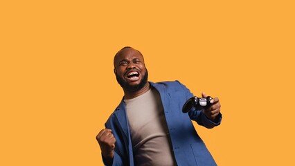 Joyous BIPOC gamer celebrating after winning gaming console game, studio background. Delighted man bragging after being victorious in videogame, defeating all enemies using gamepad, camera B