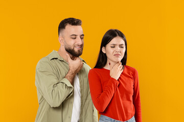Unhealthy young couple touching their necks, suffering from sore throat, yellow studio background. Cold, flu concept