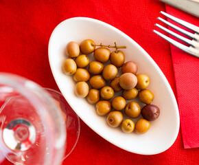 There is full bowl of green pickled olives with stone on table. Spicy addition to light alcoholic drinks, first and second courses