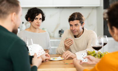 Men and women play card game poker during friendly gatherings at home. Couple enthusiastically participate in game, believe in luck, collect chips, distribute winnings