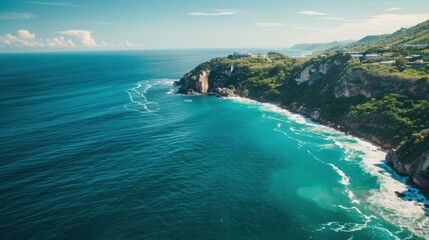 Fototapeta premium Aerial view of a pristine coastline with turquoise waters meeting rugged cliffs and sandy beaches, surrounded by lush greenery and rolling hills under a clear blue sky.