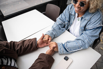 Smiling lesbian couple holding hands at a table outdoors