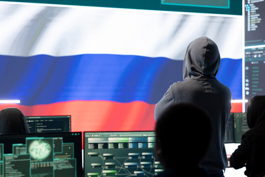 Russian hacker with a hood installing panic by misconception and manipulation, working in governmental cyber operations room. Impact of fake news and ideology propaganda in a hybrid war.