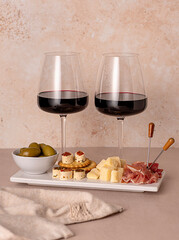 Food photography of red wine with cheese parmesan, prosciutto, olives; crackers with soft cheese; wine glasses, assortment of appetizers for a party, celebration