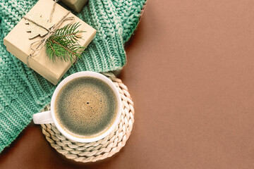 Flat lay of cup of coffee, wrapped gifts, and a green knitted scarf on a warm brown background with copy space. Color of the year 2025 - Mocha Mousse