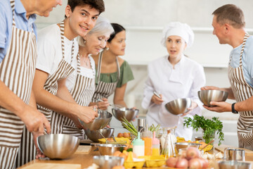 Female chef giving instructions to adult students standing around table in cooking class