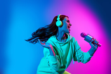Photo of cheerful pretty lady dressed sweatshirt earphones singing microphone isolated neon pink...