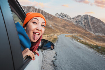 Carefree tourist enjoying road trip, sticking tongue out of car window in mountain landscape