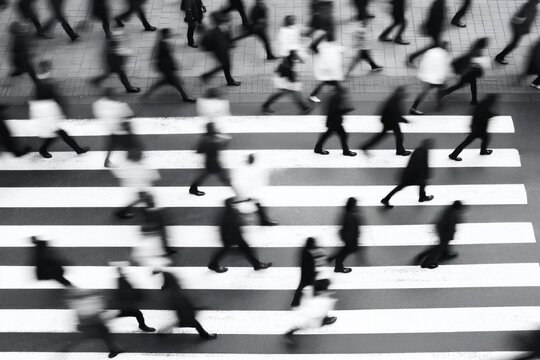 Fototapeta Blurred black, white photo of people rushing across pedestrian crossing. Busy urban scene. City life. People walking fast. Urban hustle, bustle. High speed. Street. Pedestrians. Crosswalk. Crowd.