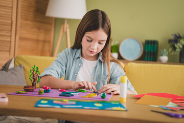 Young girl in denim shirt crafting creatively with colorful paper indoors on a sunny weekend afternoon in cozy living room