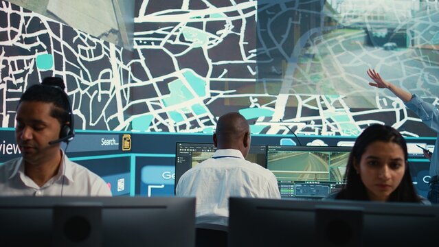 Diverse dispatch operators giving real time updates on order delivery and shipment, working in call center observation room. Employees guiding couriers around the city, CCTV footage. Camera B.