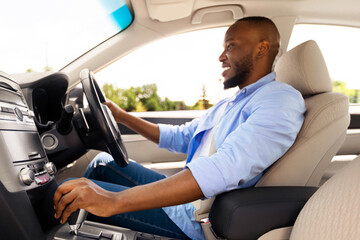 Profile side view of young African American man sitting in modern vehicle, driving his new auto,...