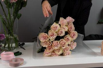 Florist arranging bouquet of bloom flowers to the order. Wrapping bouquet of rose flowers into...
