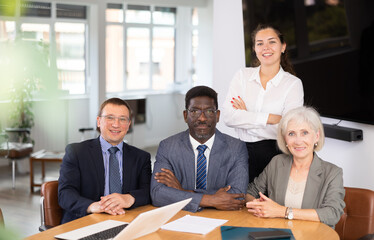 Group of different people in business suits pose sitting at table in office..