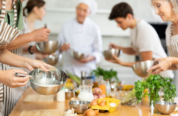 People attending group culinary classes, learning culinary skills from professional chef. Closeup of hands mixing sauce in bowl with whisk..