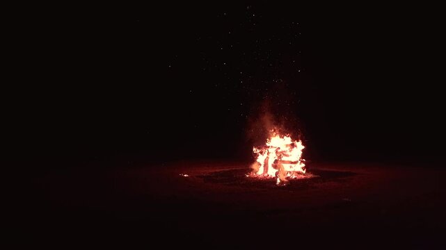 Bonfire made of logs burning with hot flames, with sparks flying. Bonfire isolated in the darkness, aligned to the right.